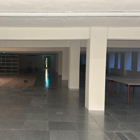 Large open-plan area showing grey tiled flooring with a central access channel and white structural columns.