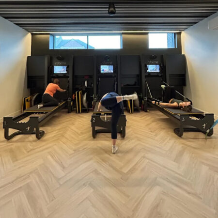 Pilates class in progress on reformer machines over herringbone LVT flooring