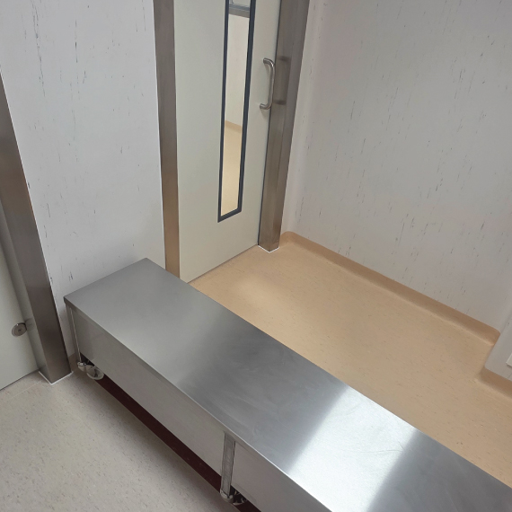 Changing room with a stainless steel step-over bench separating light grey vinyl flooring from cream vinyl flooring with coved skirting